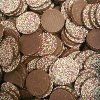 A large assortment of Mega Chocolate Jazzies, milk chocolate discs topped with colorful sprinkles.